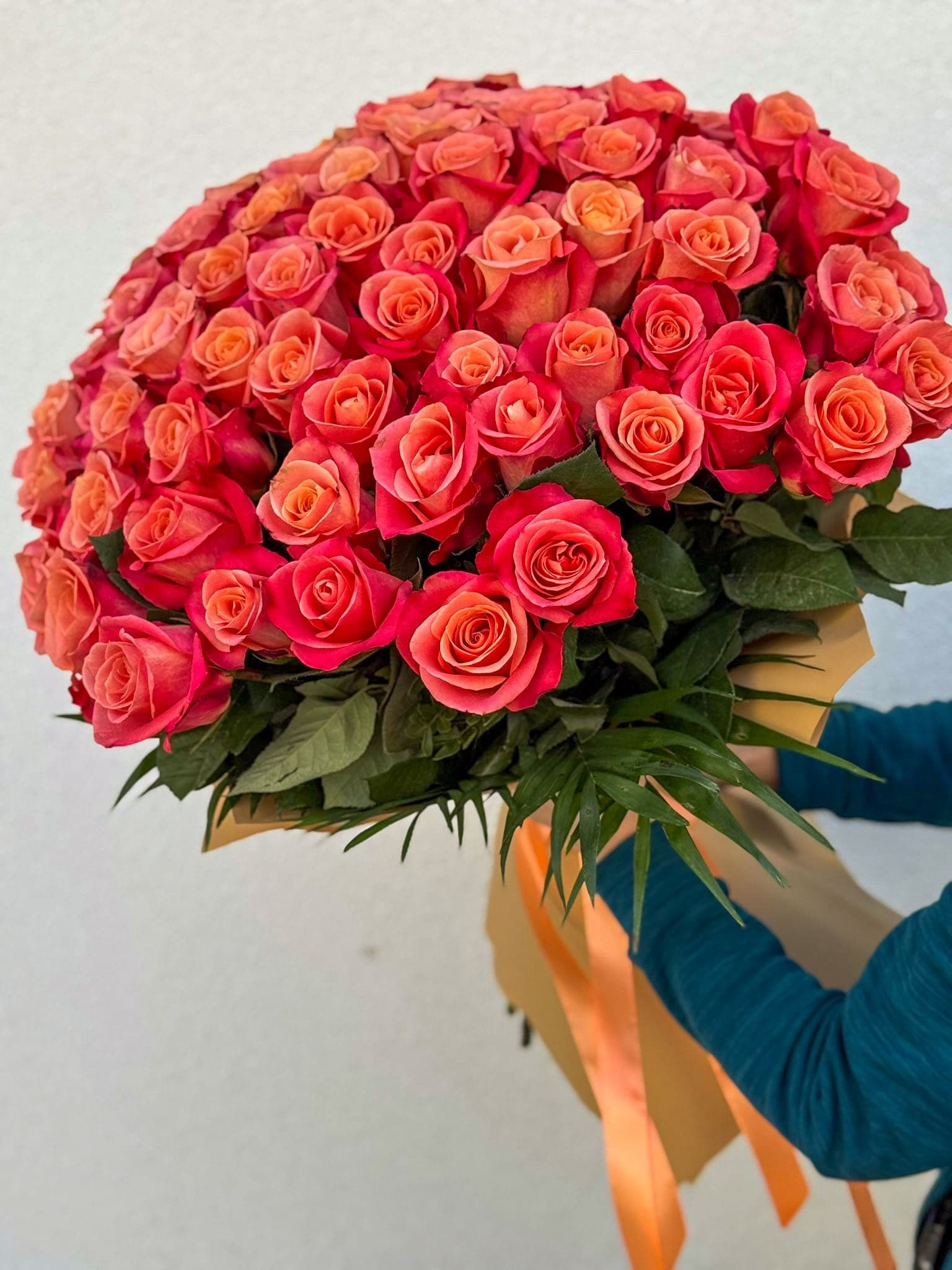 Buchet impresionant din trandafiri roz intens și corai, completat cu frunziș verde și ambalaj elegant în nuanțe naturale, cu fundă portocalie. Un buchet floral premium, ideal pentru declarații de dragoste, aniversări și surprize memorabile.