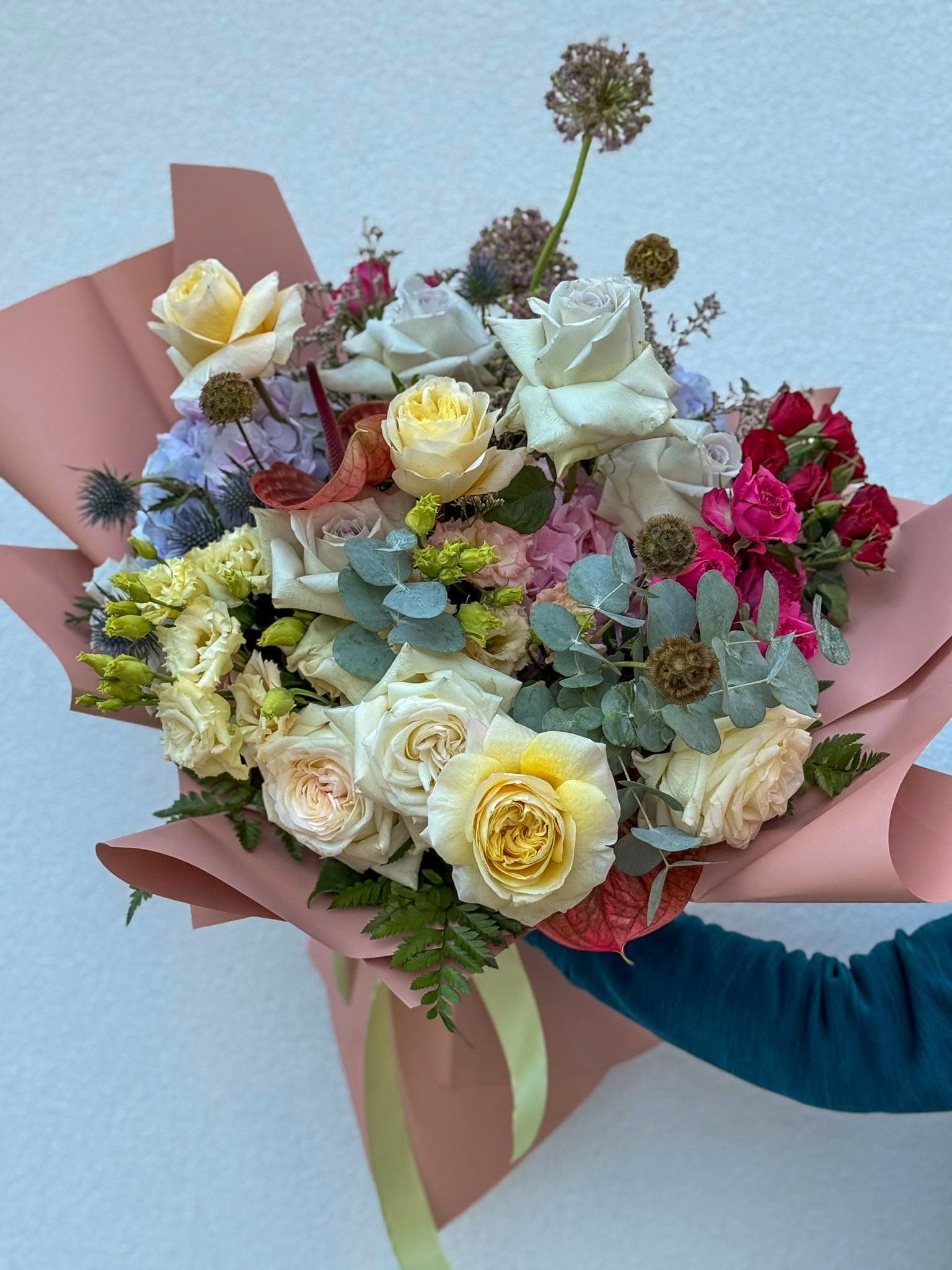 Buchet floral premium cu trandafiri albi și galbeni, trandafiri roz intens, hortensie mov și roz, eucalipt și flori decorative exotice. Un aranjament sofisticat, în ambalaj roz pudrat, ideal pentru aniversări, ocazii speciale și cadouri elegante.