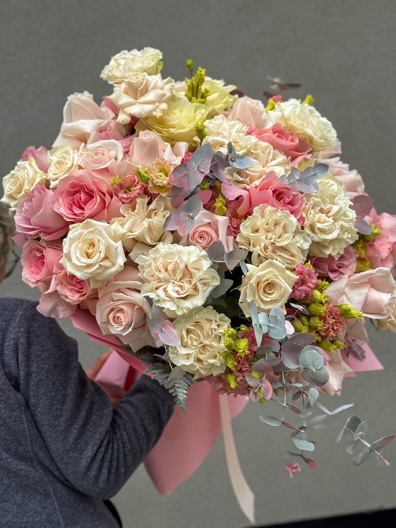 Buchet floral premium cu trandafiri roz, crem și ivoire, completat cu eucalipt argintiu și flori decorative în nuanțe pastelate. Un aranjament bogat și elegant, ambalat în hârtie roz, ideal pentru aniversări, nunți și cadouri deosebite.